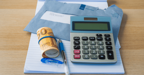 close up van een rekenmachine, rolletje geld van 50 euro, pen, kladblok en een brief van de Belastingdienst